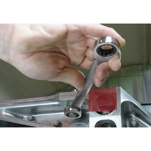 Facom ratcheting wrench SKU 64_7_8X15_16 held by hand near metal machinery, close-up view.
