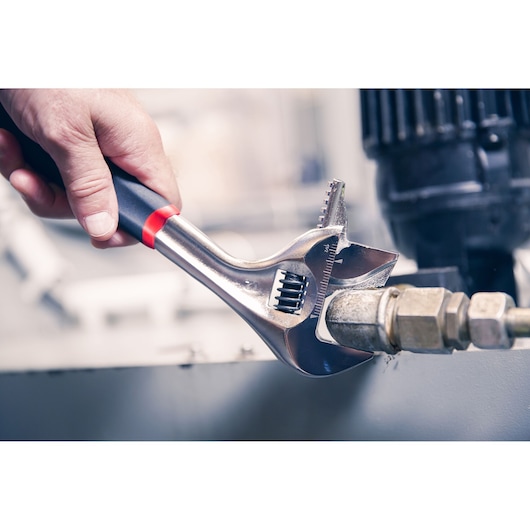 Facom adjustable wrench 101_12GR in use, tightening a metal pipe fitting, close-up photography.