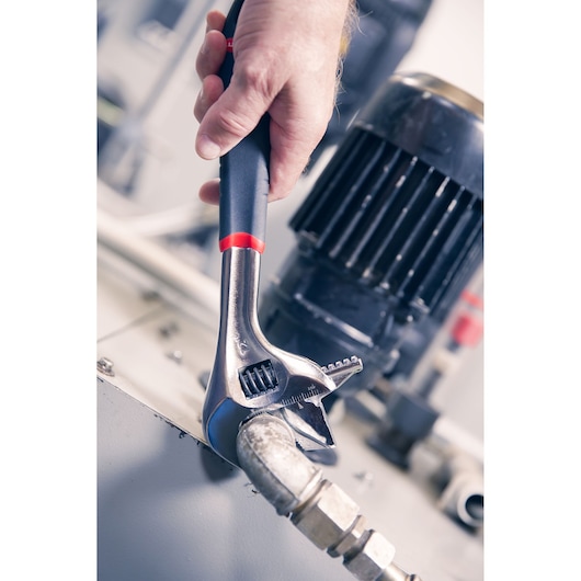Photo of Facom adjustable wrench 101_8GR gripping a metal pipe fitting, held by a hand in an industrial setting.