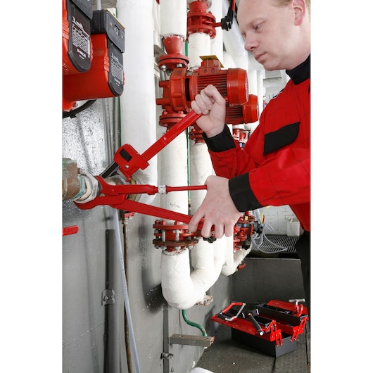 Facom 131A_10 pipe wrench in use by technician on industrial piping, red tools and toolbox visible.