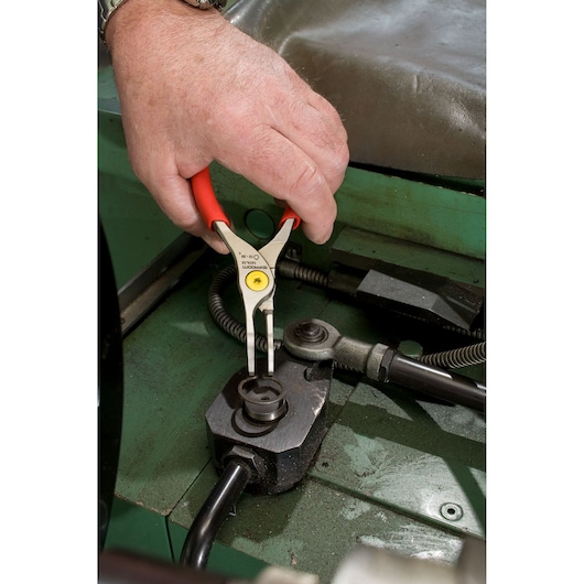 Facom 167A13 circlip pliers with red handles used to remove a circlip in an industrial machine close-up.