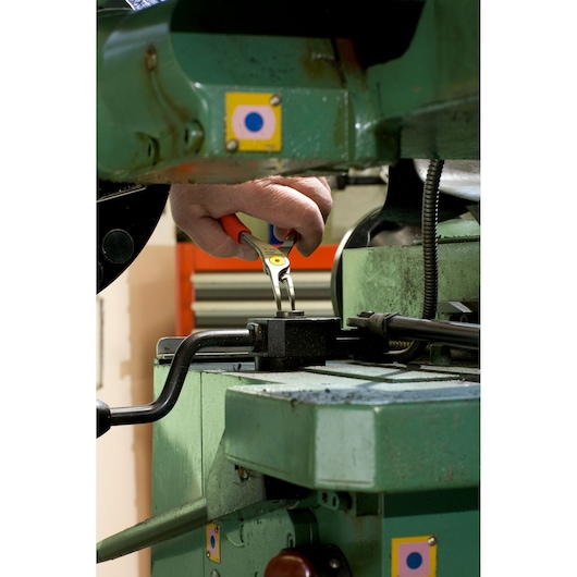 Facom pliers 167A18 held by a hand, used to adjust a part on green industrial equipment, close-up action.