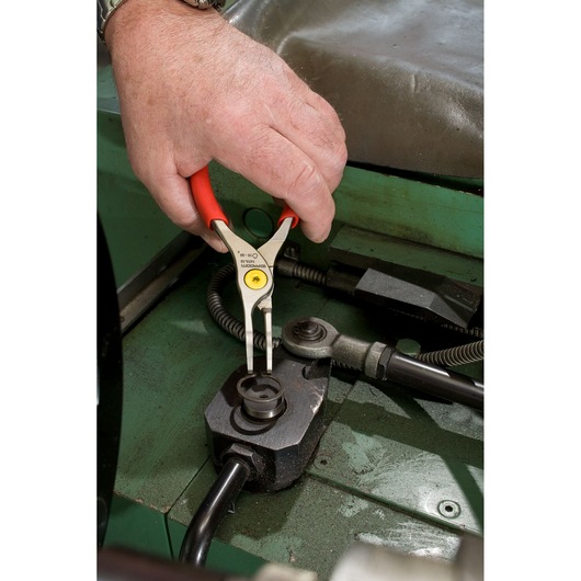 Facom 167A23 pliers with red handles used to manipulate machinery part, photo with close-up angle.