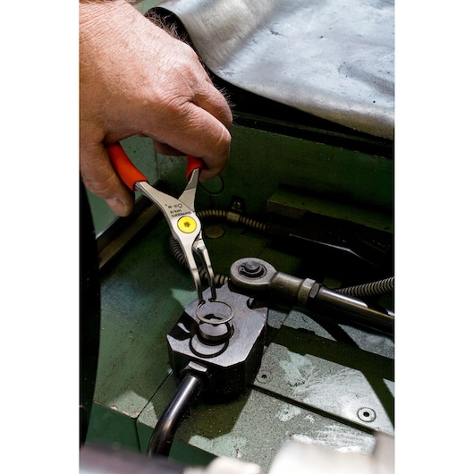 Facom 167A9 snap ring pliers with red handles held by hand working on machinery, close-up photography.