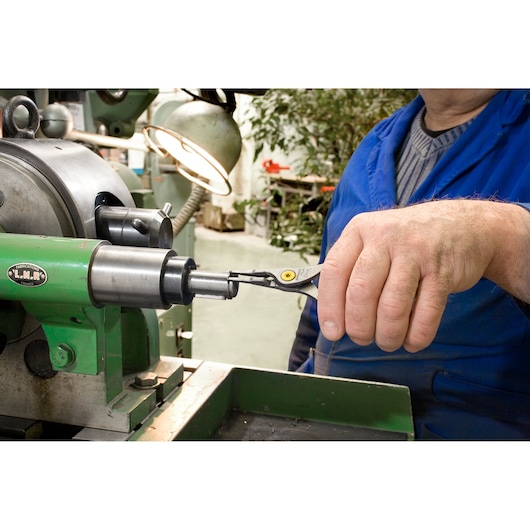 Facom 177A18 snap ring pliers used by worker in blue uniform on industrial machine.