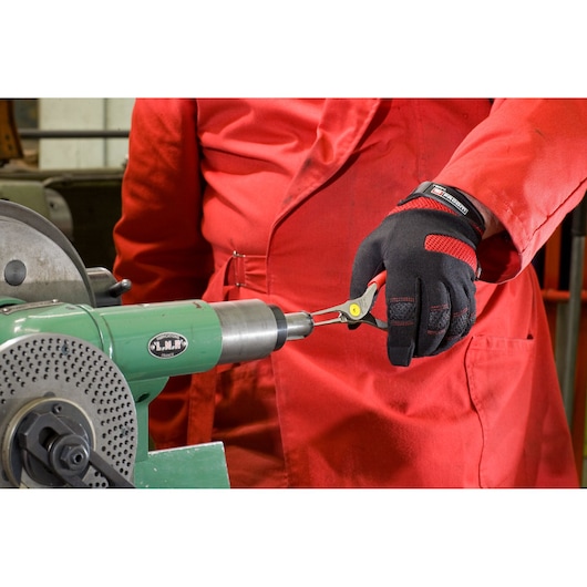 Photo of Facom 177A23 pliers held by a gloved hand in front of industrial machinery.