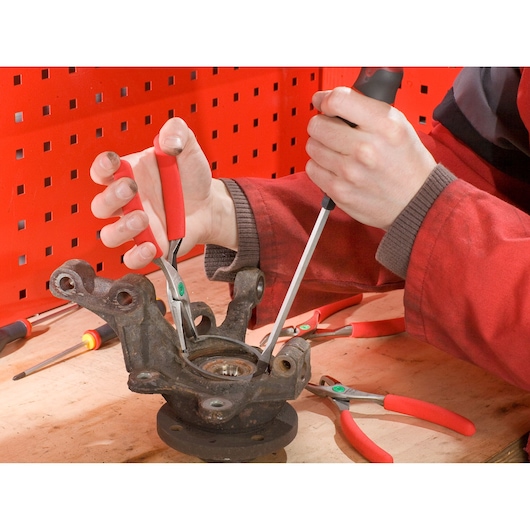 Facom 179A18 pliers with red handles used on a metal component, workshop setting, close-up angle.