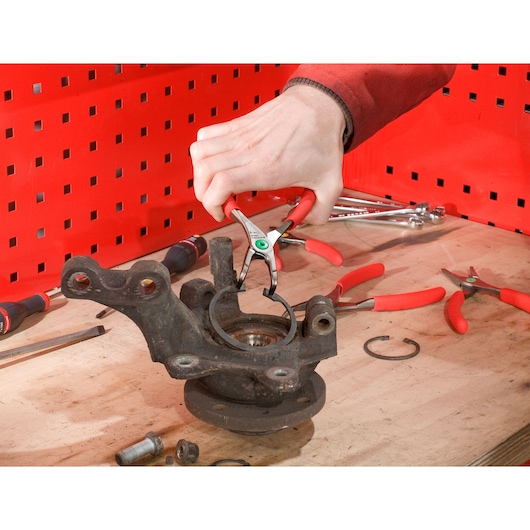 Facom 199A_18 circlip pliers removing a retaining ring from an automotive part on a workbench.