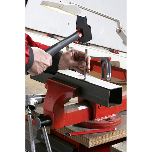 Facom 200C_42 hammer used to strike punch on metal tube held in red bench vise, workshop setting.