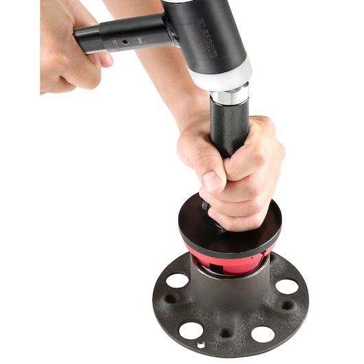 Photo of Facom pipe tool 21750 in use on a metal flange, close-up with hands holding the tool.