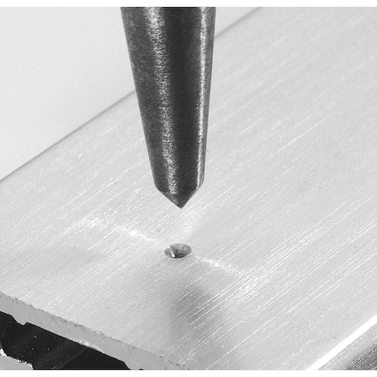 Facom 257.GPB center punch tip marking a metal surface, close-up angle, photography.