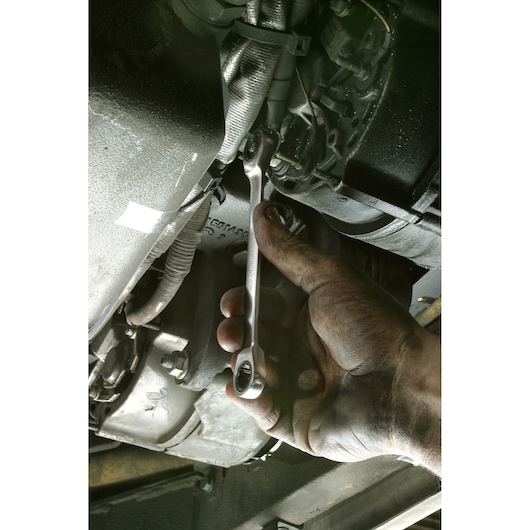 Facom 64_21X23 ratcheting combination wrench being used on a bolt in an engine bay by a dirty hand.