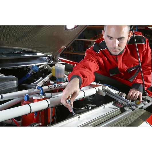 Facom 64_21X23 combination wrench used by mechanic in red coveralls working on car engine.