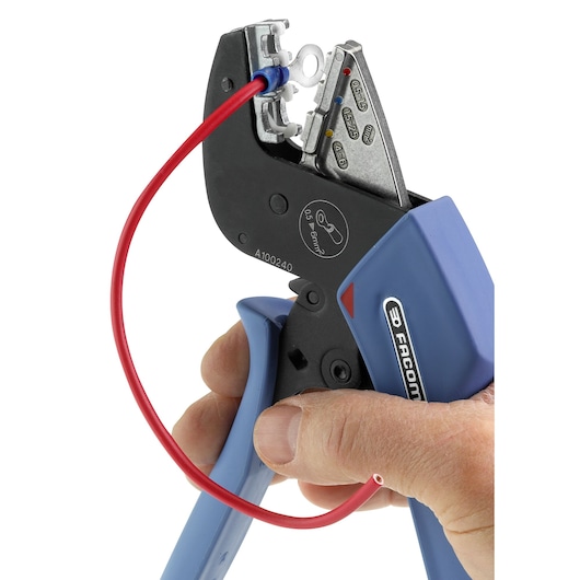 Facom crimping tool 673838 held by hand, blue handles, crimping red wire, close-up with white background.