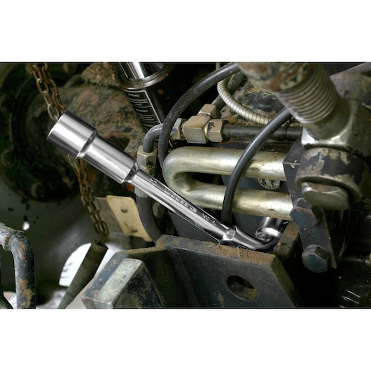Facom 75_26 socket wrench in use tightening a bolt on machinery, surrounded by metal hoses and fittings.