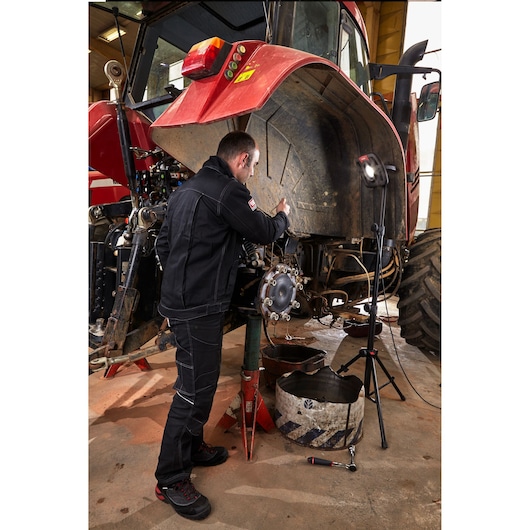 Facom 779_TRIPOD photography tripod shown supporting a work light next to a mechanic repairing a red tractor.