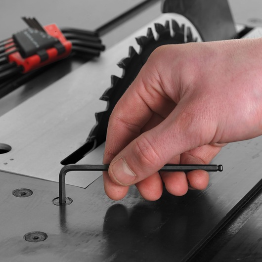 Facom 83SH_10 hex key set used near a table saw, close-up of hand adjusting with black L-shaped tool.