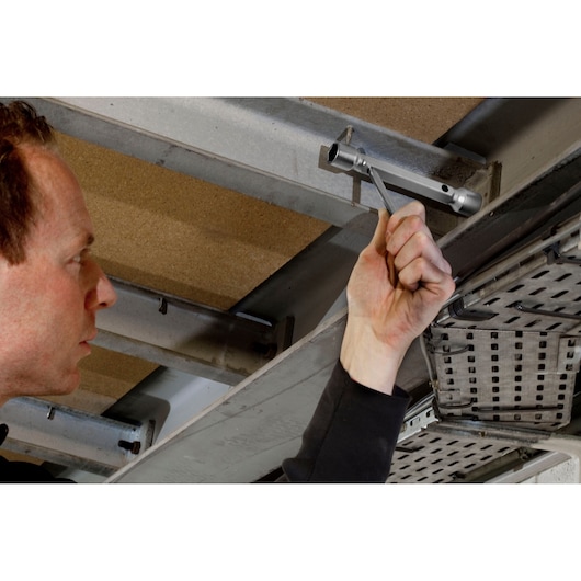 Facom 97_14X15 offset box wrench used on overhead metal framework, hand gripping tool for assembly task.