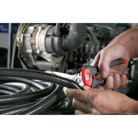 Facom 980C cable cutter with red and black handle cutting black corrugated tubing near engine