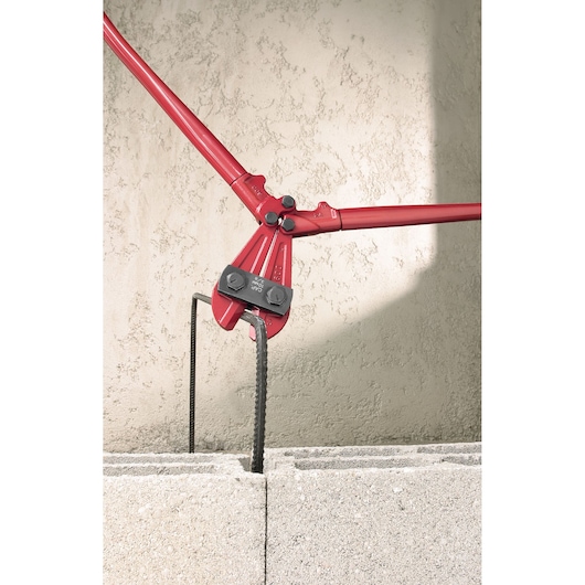 Facom 990B4 bolt cutter with red handles cutting rebar in concrete block, side view.