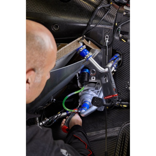 Photo of a Facom ATPA4V.J12IPB tool used by a technician working on automotive engine components with visible wiring and hoses.