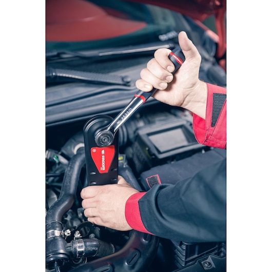 Photo of Facom AXS.SPB ratchet wrench being used in automotive engine compartment, hand gripping tool handle.