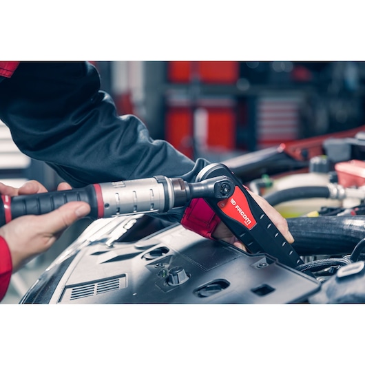 Facom AXS.SPB cordless ratchet in use on a car engine, close-up in automotive workshop.