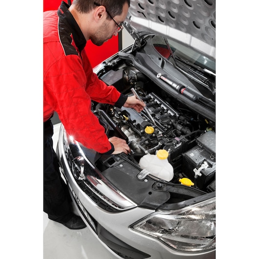 Facom BJ14BH2 photography of mechanic using tool under car hood, red and black uniform visible.