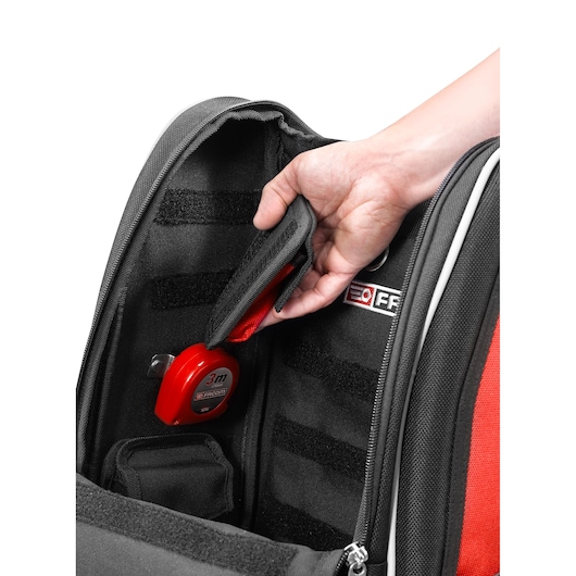 Photo of Facom BS.MCBPB tool bag interior with hand accessing internal pocket, red measuring tape secured inside.