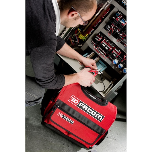Photo of Facom red tool bag BST14PB near electrical cabinet, technician using tools.