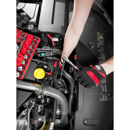 Photo of Facom C.48-J2PB socket set in use, gloved hands working with a ratchet on a car engine, top view.