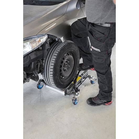 Facom CR_12H wheel dolly in use, supporting a car tire with blue casters, side angle, workshop setting.