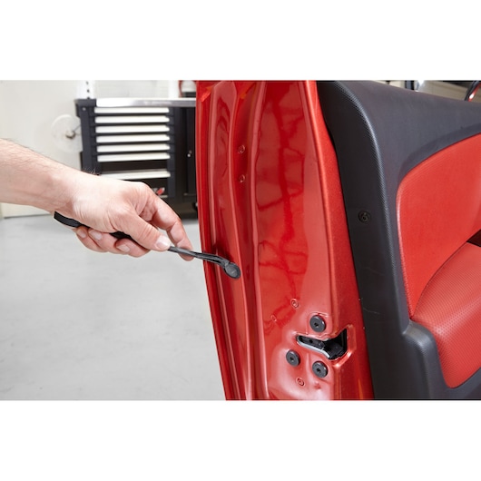 Facom CR.LPTPB automotive trim removal tool in use removing a fastener from a red car door interior.