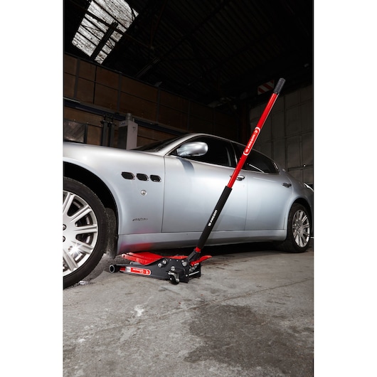 Facom DL_2LP low profile hydraulic floor jack in red and black lifting a silver car in a garage, side view.