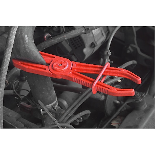 Facom DM_34GM red hose clamp plier holding a hose in an engine bay, close-up photography.