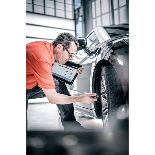 Facom DX_TSCANPB automotive diagnostic tool in use on car tire, person holding tablet and sensor.