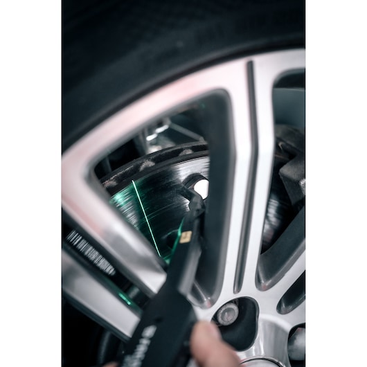 Facom DX_TSCANPB tool measuring car brake disc through alloy wheel with green laser, close-up angle.