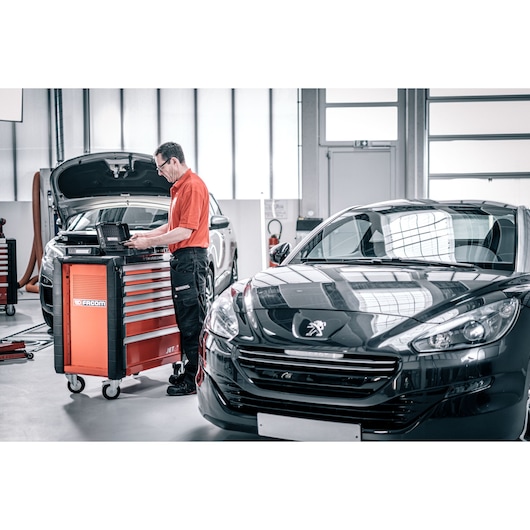 Facom DX_TSCANPB tool cabinet in garage next to cars, technician using diagnostic laptop, photo of workshop scene.