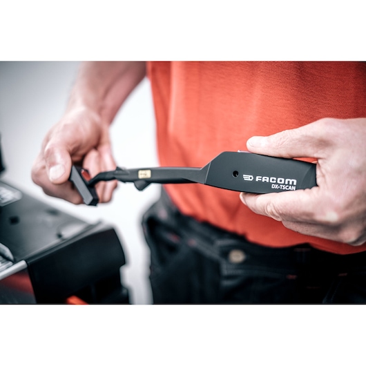 Close-up photo of Facom DX_TSCANPB tool held in hand, black ergonomic design with visible branding.