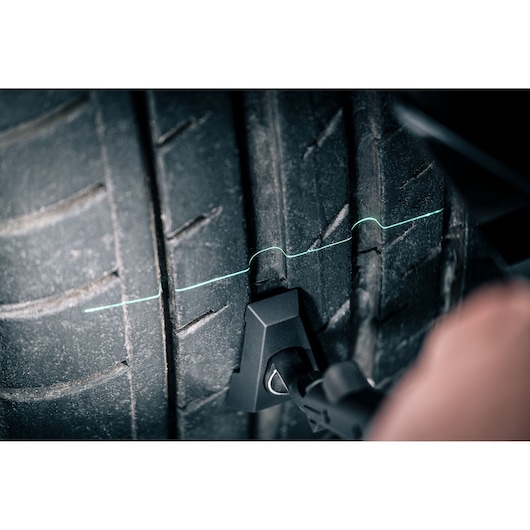 Facom DX_TSCANPB tire tread scanner measuring tire wear with green laser line on tire surface, closeup.