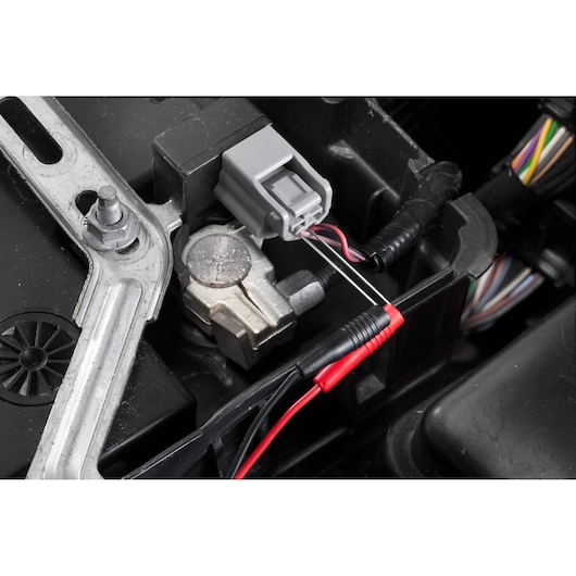 Facom DX.V12PB multimeter probes testing car electrical connector close-up.
