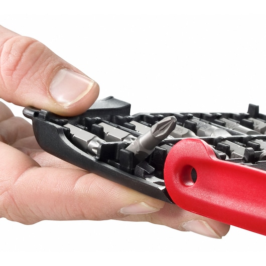 Close-up of a hand selecting a screwdriver bit from a Facom bit set, showing a black plastic case with various bits and a red handle.