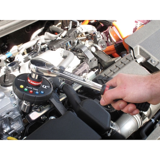 Facom torque wrench E506-340S used on car engine, close-up with hand gripping handle.