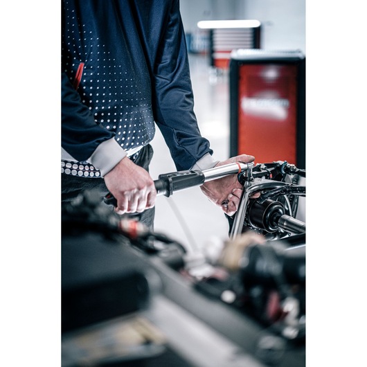 Photo of hands using Facom E_516ST-135PB torque wrench on automotive part in a workshop setting.