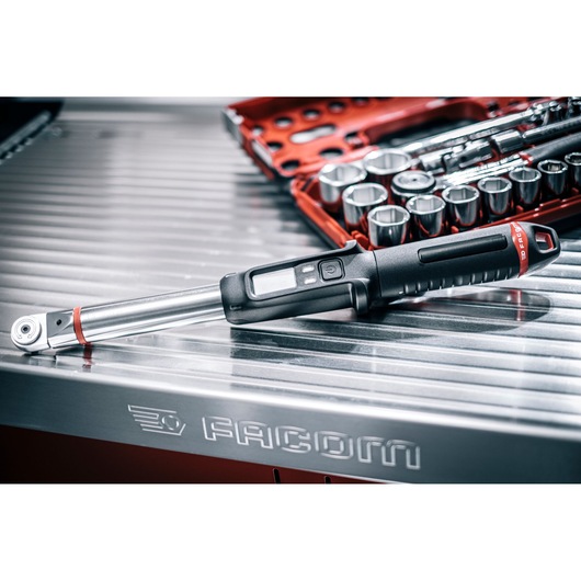 Facom E_516ST-135PB digital torque wrench on metal workbench with socket set in background.