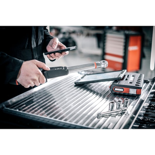 Facom E_516ST-340PB torque wrench in use with tablet and sockets on metal workbench, angled view.