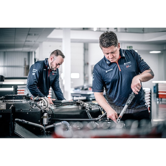 Facom E_516ST-340PB torque wrench used by technicians working on an automotive engine in a workshop.