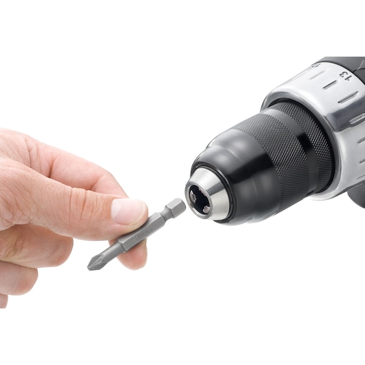 Facom E612PB screwdriver bit held by hand near drill chuck, close-up on white background.