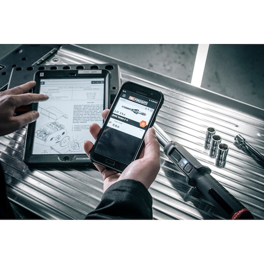 Facom E_516ST-30PB smart torque wrench with digital display, sockets, phone, and tablet on metal workbench.