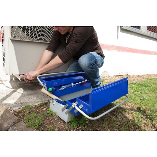 Facom E010201 metal tool box with blue compartments open beside technician working outdoors.